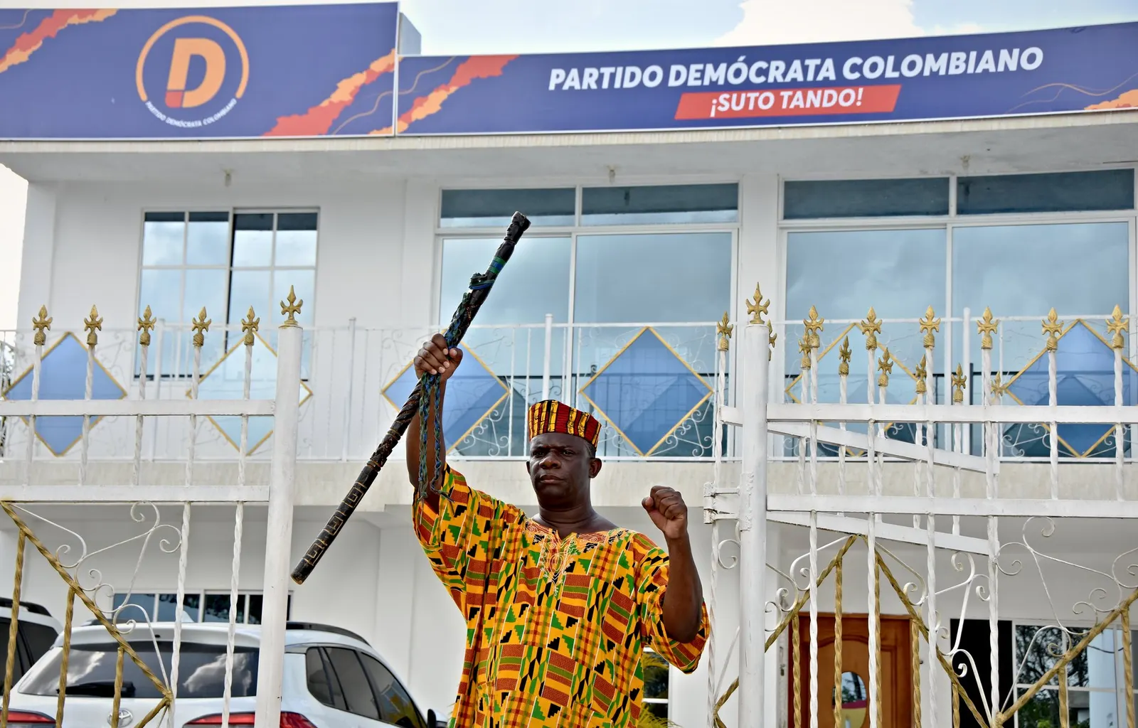 Pedro Adán Torres, con camisa de estampado africano, levanta un bastón de mando frente a la sede del Partido Demócrata Colombiano en San Basilio de Palenque