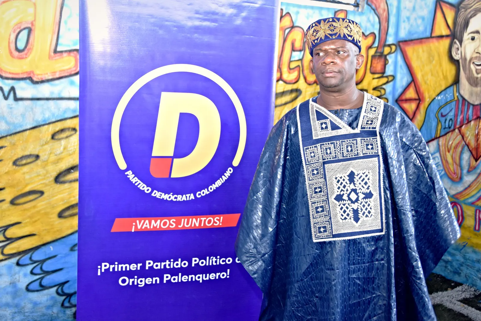 Pedro Adán Torres, con túnica azul bordada, junto al telón «Primer partido político de origen palenquero» y el logo del partido